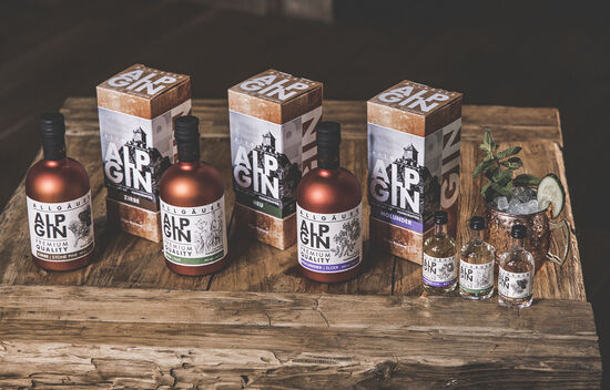 Die AlpGin-Serie in den Sorten Heu, Holunder und Zirbe, präsentiert in kupfernen Flaschen