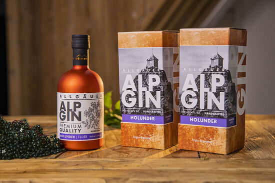 Der AlpGin Holunder wird präsentiert auf einem rustikalen Holztisch und neben dunklen Holunderbeeren