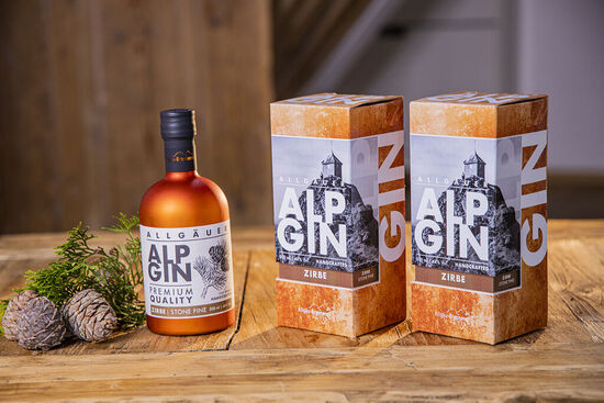 Eine Flasche AlpGin ZIrbe steht auf einem rustikalen Holztisch. Daneben befinden sich Zirbelkiefer-Zapfen.