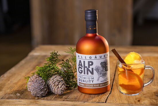 Der Glühgin wird präsentiert in einer Glastasse, garniert mit einer Stange Zimt und nebenan die Flasche AlpGin Zirbe.