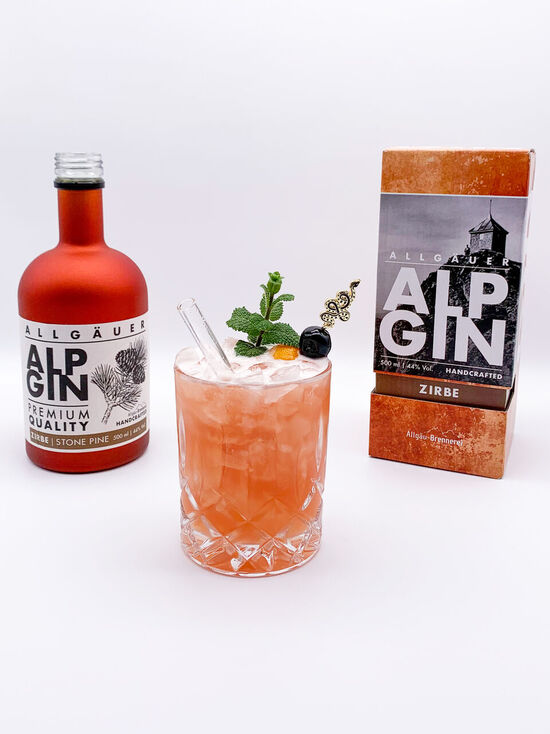 Der AlpGin Zirbe steht neben einem orangefarbenen Cocktail, dem exotischen Allgäuer!