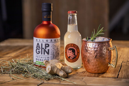 Eine kupferne Flasche AlpGin Heu präsentiert mit einer Flasche Thomas Henry Spicy Ginger und einem kupfernen Cocktailbecher.